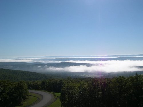 A scenic view of rolling hills and valleys shrouded in mist under a clear blue sky.