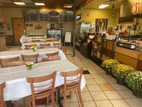A cozy diner interior with white tablecloths, flowers on tables, and a counter displaying food and drinks.