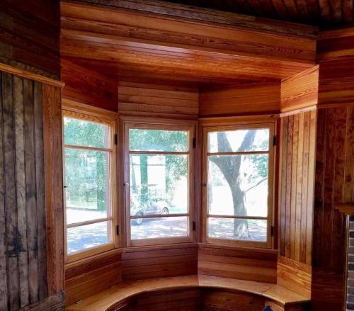 Cozy wooden nook with large windows, showcasing natural light and views of trees outside.