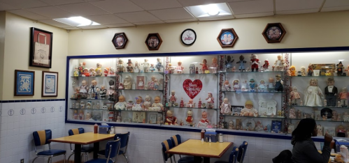 A cozy diner interior featuring a display case filled with various dolls and vintage decor on the walls.