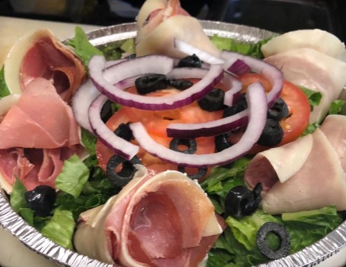 A fresh salad with lettuce, sliced tomatoes, olives, and rolled slices of ham and turkey, topped with red onion rings.