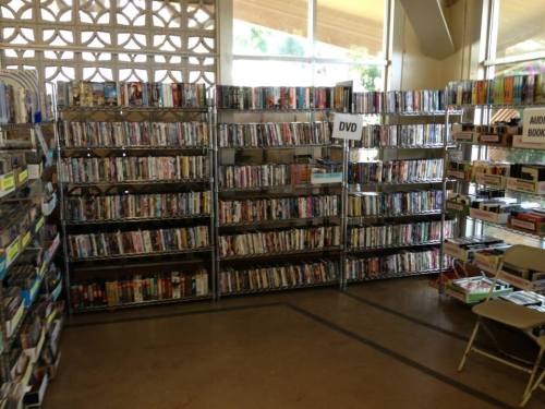 A spacious library corner filled with shelves of DVDs and books, with tables and chairs for reading.