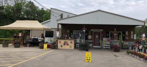 A welcoming garden center with a tent, flowers, and a cozy building under a cloudy sky.