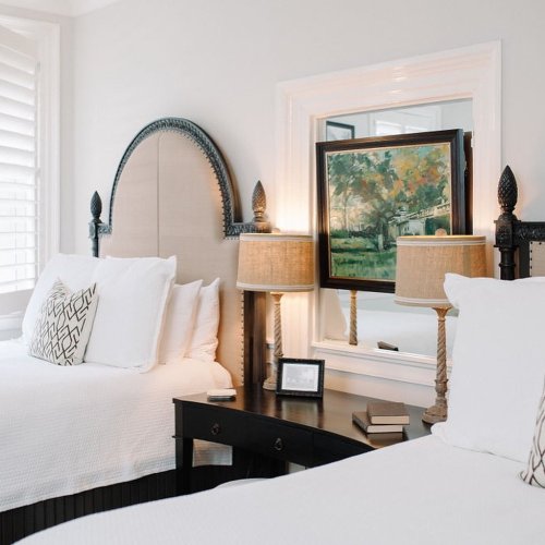 A bright bedroom with two beds, decorative lamps, a mirror, and a colorful painting on the wall.