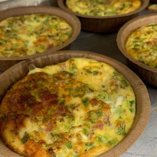 Baked frittatas in brown paper cups, featuring green vegetables and a golden, fluffy texture.