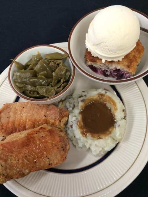 A plate featuring two pieces of fried fish, mashed potatoes with gravy, green beans, and a dessert with ice cream.