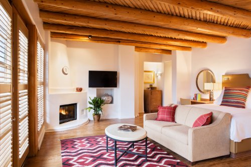 Cozy hotel room with wooden beams, a fireplace, a TV, a sofa, and colorful decor, featuring a warm and inviting atmosphere.