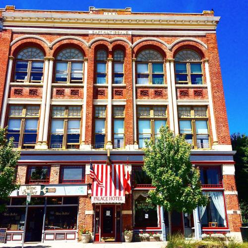 Historic brick building with large windows, featuring the Palace Hotel sign and red and white striped awning.