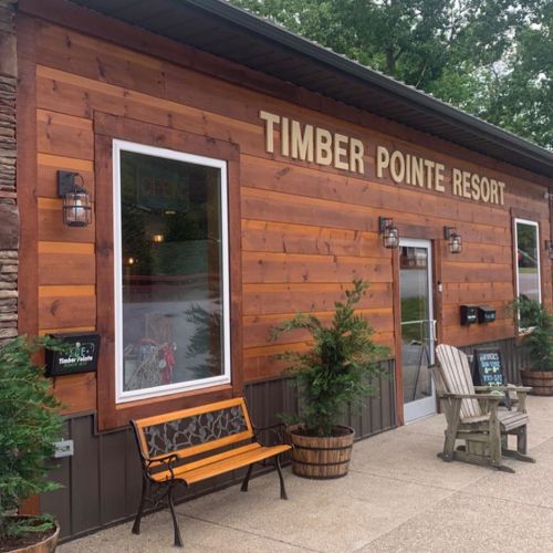 Exterior of Timber Pointe Resort featuring wooden siding, a welcoming sign, and a bench in front.