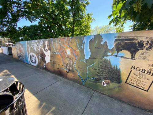 A colorful mural depicting a map and animals, featuring a dog and trees, on a wall in an outdoor setting.
