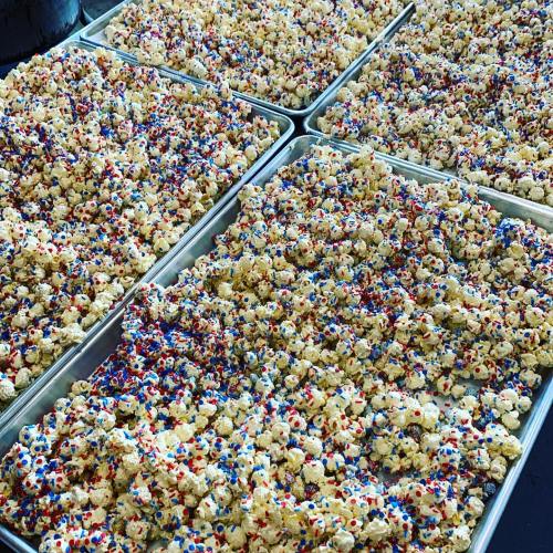 Trays of popcorn coated in white chocolate and colorful red, white, and blue sprinkles.