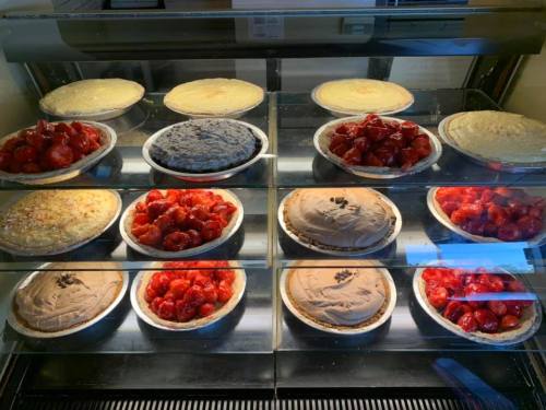 A display case filled with various pies, including strawberry, chocolate, and cream pies, arranged neatly on plates.