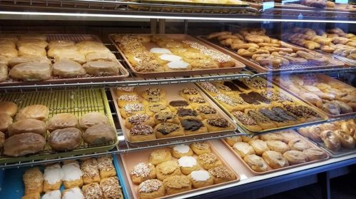 A display case filled with various pastries, including glazed donuts, cream-filled treats, and sprinkled desserts.