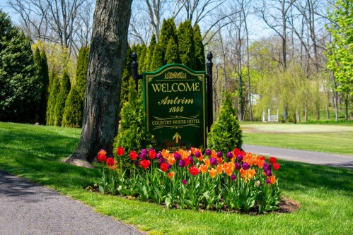 A welcome sign for Antrim 1844 Country House Hotel, surrounded by colorful tulips and lush greenery.