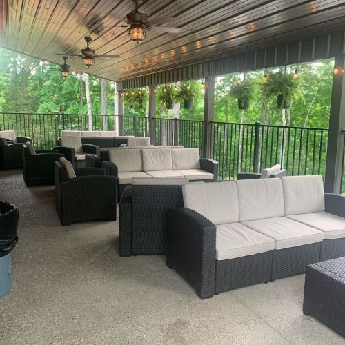A covered outdoor seating area with black wicker couches and green foliage in the background.