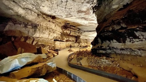A winding path through a large, rocky cave with textured walls and scattered stones.
