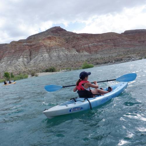 A person kayaking on a river with rocky hills in the background, enjoying a sunny day outdoors.