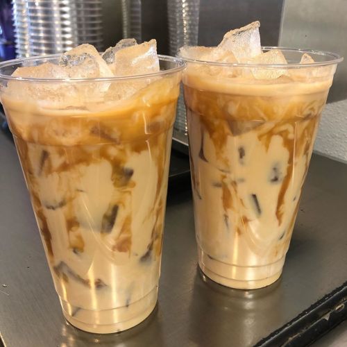 Two clear cups filled with iced coffee, layered with cream and ice cubes, sitting on a counter.
