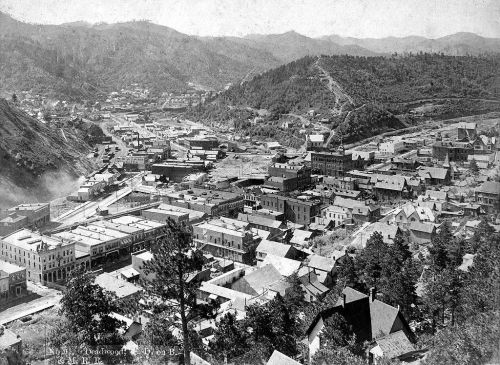 Aerial view of a historic town surrounded by hills, featuring buildings and streets in a valley setting.