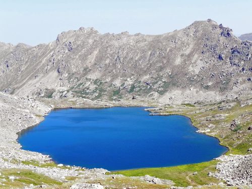 A serene blue lake surrounded by rocky mountains and grassy terrain under a clear sky.