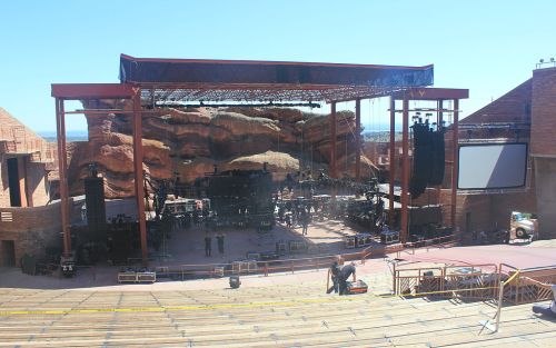 A large outdoor concert stage at Red Rocks Amphitheatre, with rocky formations in the background and empty seating.