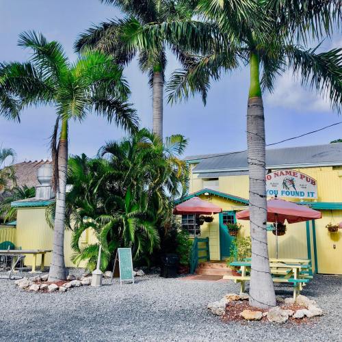A colorful pub surrounded by palm trees and greenery, featuring outdoor seating and a welcoming entrance.
