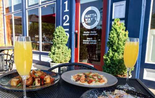 Brunch spread with mimosas, featuring dishes of roasted potatoes and a creamy pasta, outside Hattaway's restaurant.