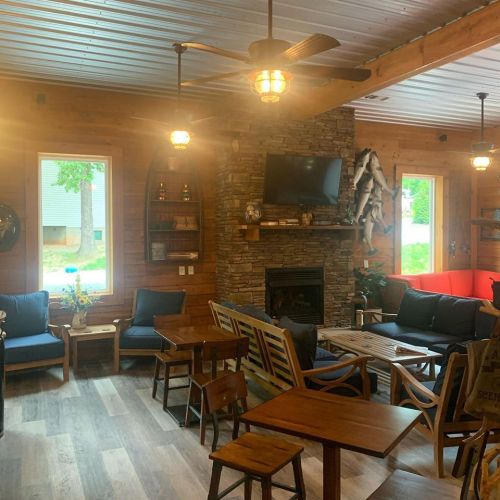 Cozy interior of a rustic cabin with wooden furniture, a stone fireplace, and large windows letting in natural light.
