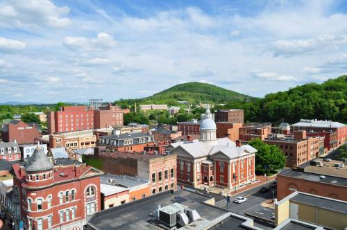 Aerial view of a small town with historic buildings, green hills, and a blue sky with scattered clouds.