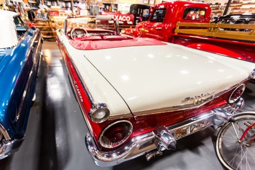 A classic convertible car with a red and white exterior, parked in a vintage car showroom.