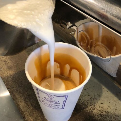 A barista pours steamed milk into a cup of espresso, creating a creamy coffee drink.