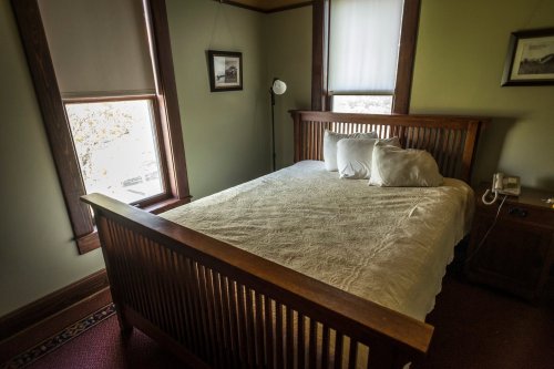 Cozy bedroom with a wooden bed, white bedding, and natural light from two windows.