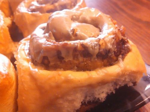 Close-up of a cinnamon roll with creamy icing, showcasing a bite taken out of the soft, fluffy pastry.