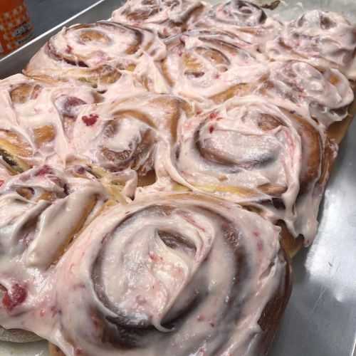 A tray of freshly baked cinnamon rolls topped with creamy pink frosting.