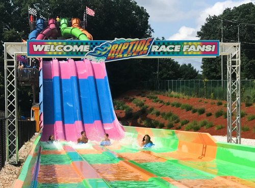 Four people splash down a colorful water slide at a water park, with a sign welcoming visitors above.
