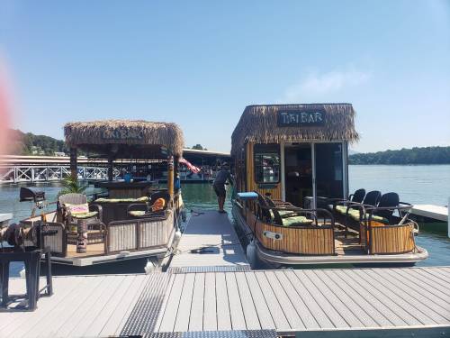Two tiki bar boats docked at a marina, with a person walking between them on a sunny day.