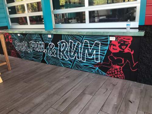 Colorful mural featuring the text "Sun, Fun & Rum" alongside a stylized illustration of a woman.