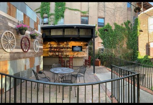 A cozy outdoor bar area with a wooden bar, seating, and greenery on the walls, surrounded by a black fence.