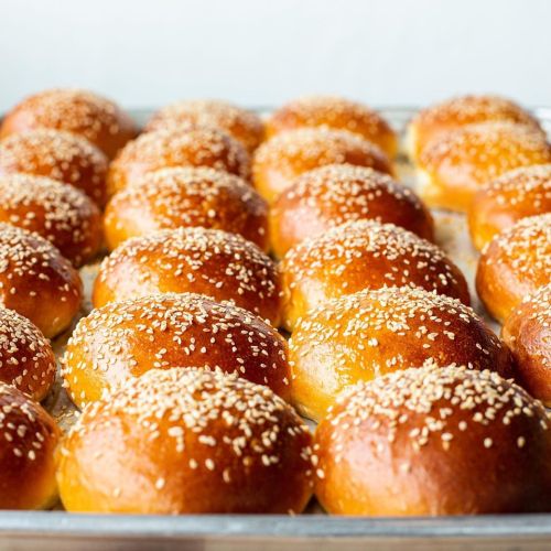 A tray of golden-brown sesame seed buns, freshly baked and arranged in neat rows.