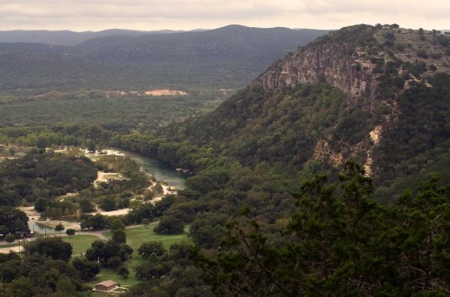 A scenic view of a river winding through lush green hills and trees under a cloudy sky.