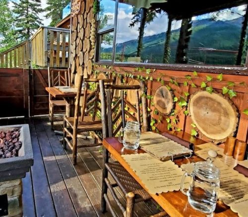 Cozy wooden restaurant interior with natural decor, featuring tables, chairs, and scenic mountain views.