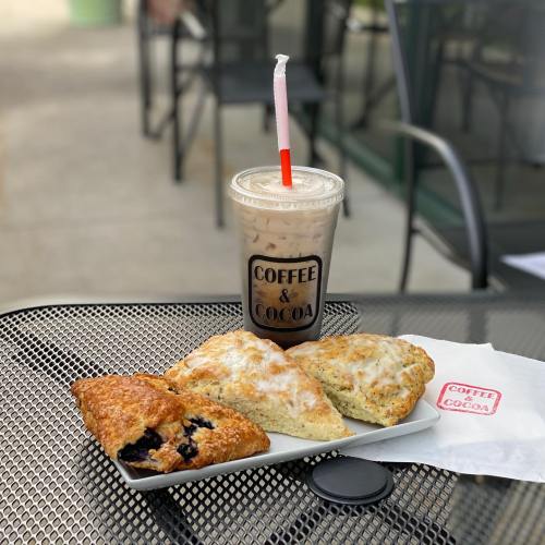 A plate with two scones and an iced coffee drink on a table, with a "Coffee & Cocoa" logo visible.