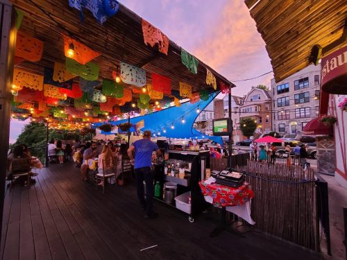 A vibrant outdoor restaurant with colorful decorations, string lights, and diners enjoying the evening atmosphere.