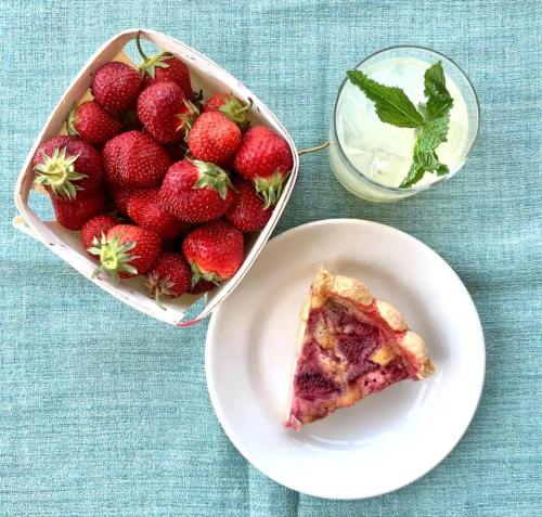 A basket of fresh strawberries, a slice of pie on a plate, and a mint garnish drink on a teal tablecloth.
