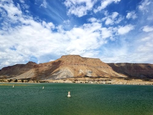 A serene lake with green water, surrounded by rocky cliffs and a blue sky filled with clouds.