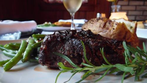 A plate featuring a juicy steak, green beans, a baked potato, and a glass of wine in a cozy dining setting.
