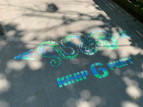 A colorful snake design on pavement with the text "KEEP 6 FEET" below it, promoting social distancing.