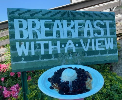 A sign reading "Breakfast with a View" next to a plate of pancakes topped with blueberries and ice cream.