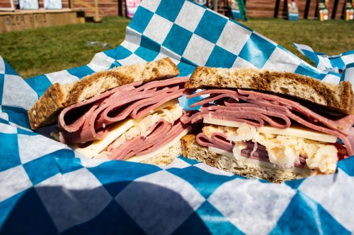 A close-up of a sandwich with layers of deli meats and cheese, wrapped in blue and white checkered paper.