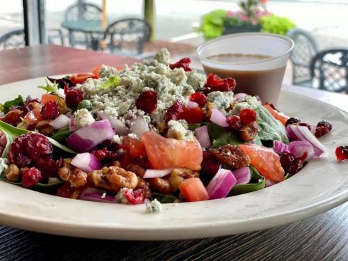 A colorful salad with greens, tomatoes, onions, cranberries, and blue cheese, served with a dressing on the side.